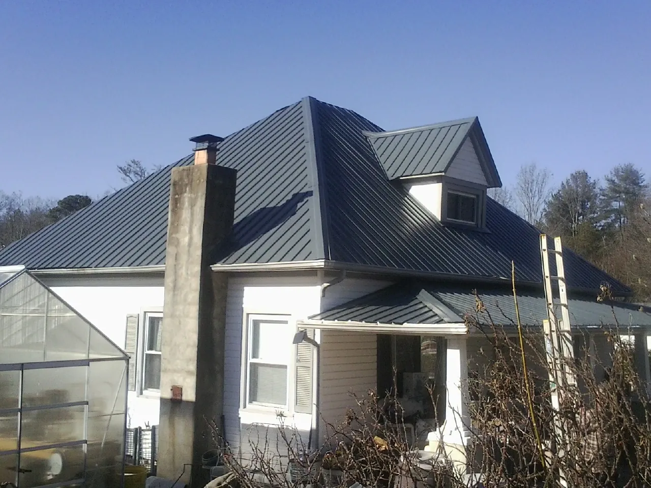 Dark blue standing seam metal roof on a white farmhouse with dormer — Slate & Tile Roof Repair by Roofing Brothers in Francestown