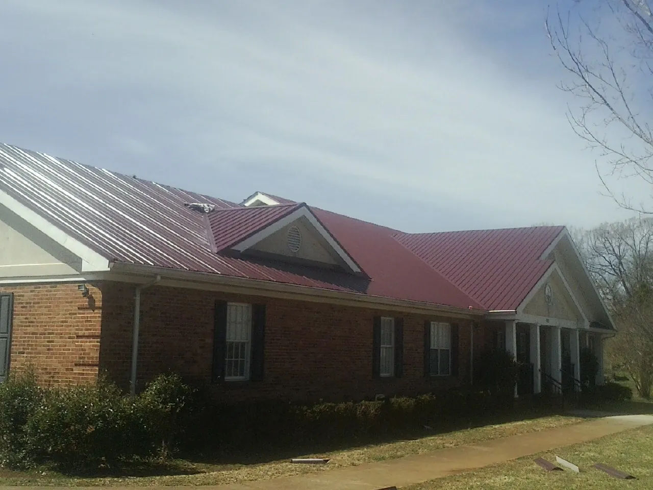 Red metal roof with gabled entries on a long brick building, from a Hail Damage Roof Repair job in Francestown