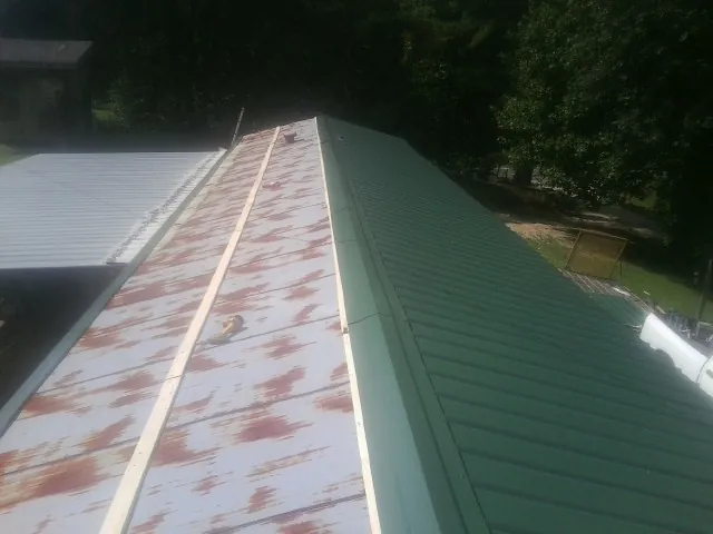 Old rusted panels beside newly installed green metal roofing — Wind Damage Roof Repair by Roofing Brothers in Francestown