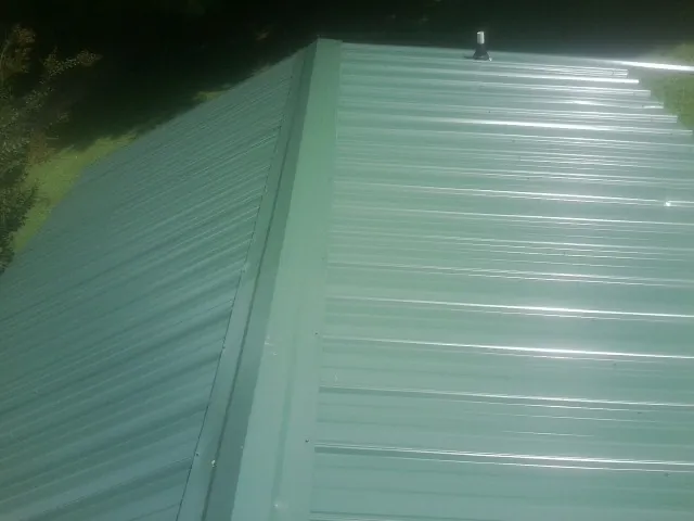 New green metal panels meeting at the ridge of a roof — Flat Roof Repair work by our crew in Francestown