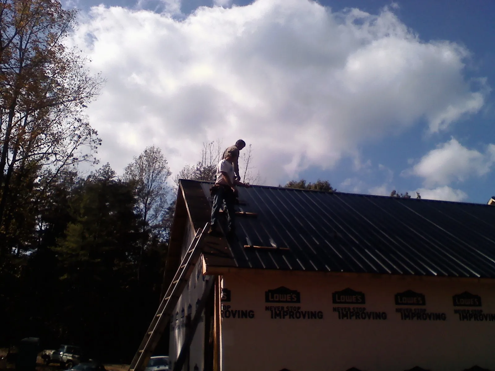 Roofer fastening dark metal panels high against a cloudy sky, from a Roof Inspection job in Francestown