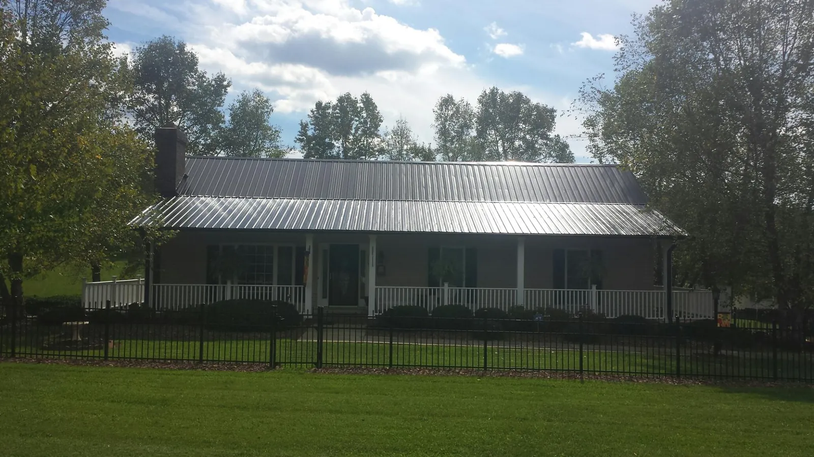 Gray metal roof on a brick ranch with a full width front porch — Gutter Guard Installation work by our crew in Francestown