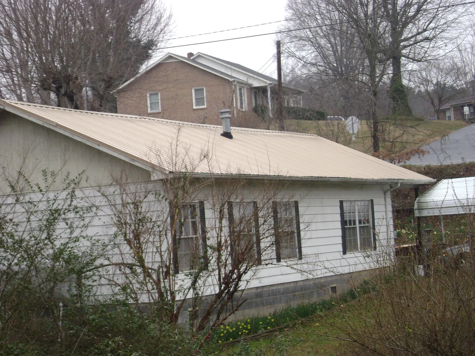 Tan metal roof on a white sided house set into a hillside — Commercial Roofing by Roofing Brothers in Francestown